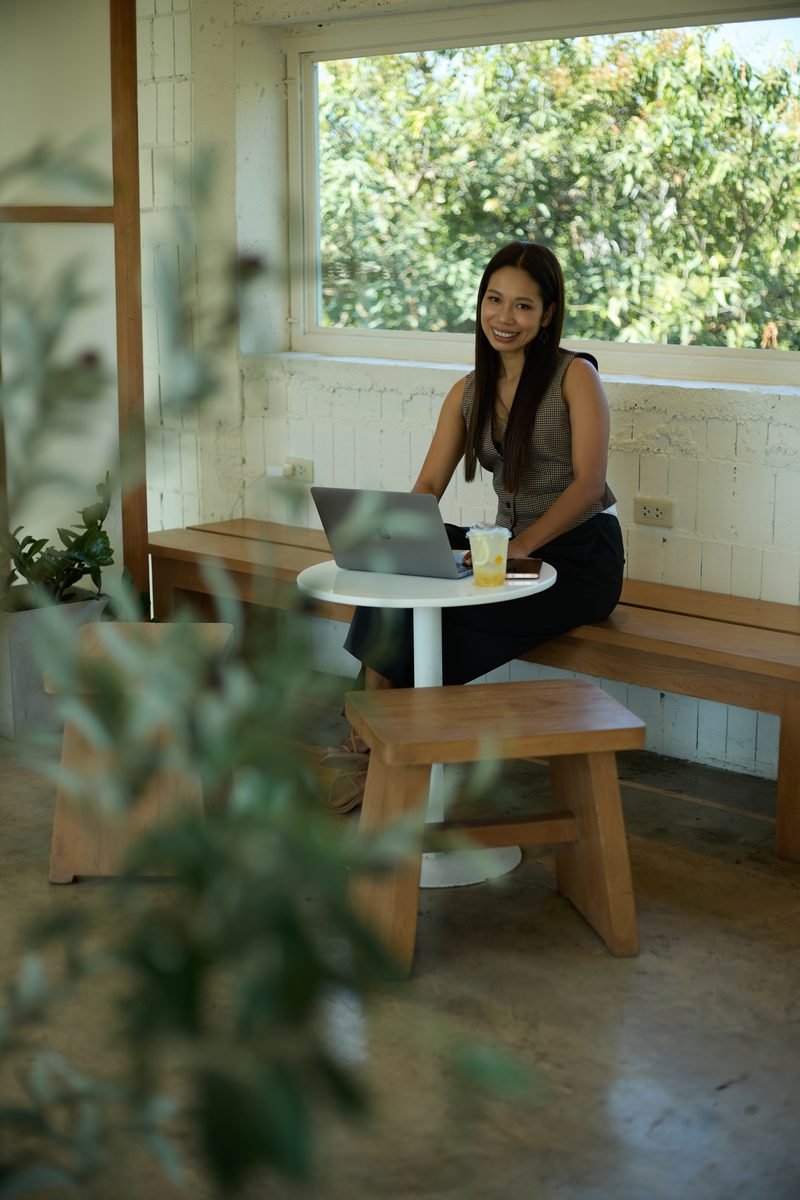 Fon Ward working on her laptop at a cafe window bench, SEO consultant for cleaning businesses